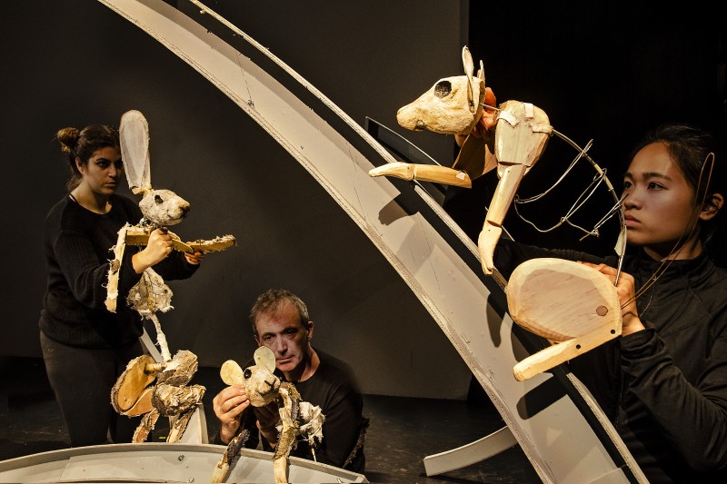 Three puppeteers manipulating three puppets of an animalistic nature.